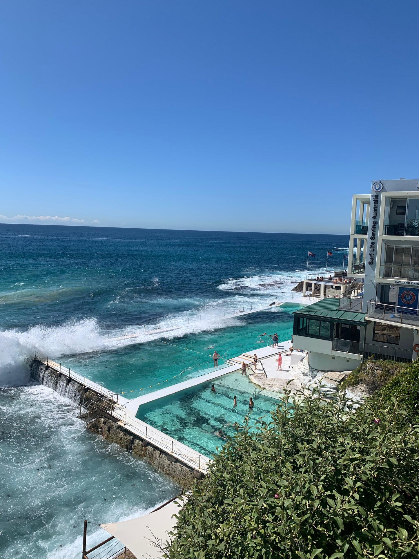 A high-quality photograph of the iconic Icebergs Pool at Bondi Beach, New South Wales (NSW), showcasing the stunning contrast between the vibrant blue waters of the pool and the crashing waves of the ocean. The image captures the beauty of the pools set against the rugged coastal landscape, with the clear sky and beach in the background. Printed on premium material for a refined and elegant finish, this photograph is a sophisticated depiction of one of Australia's most famous swimming spots.